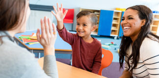 Boy raising hand in classroom with mom and teacher