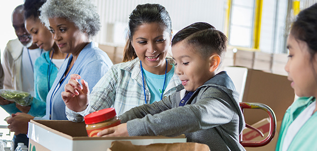 Food bank volunteers sort out food donations Mid adult mom and her elementary age son sort food items received during a food drive. The little boy is placing a jar of peanut butter into a donation box.