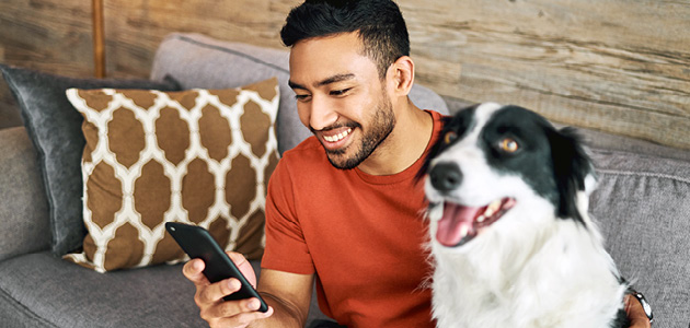 Man looking at mobile phone in his right hand with dog beside him